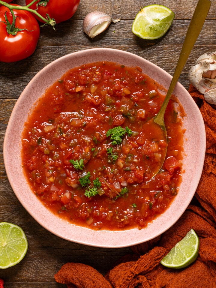 Bowl of salsa with a spoon on a wood table.