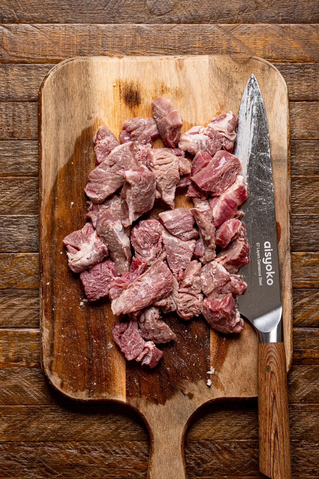 Ribeye steak being chopped into chunks on a cutting board with a knife.