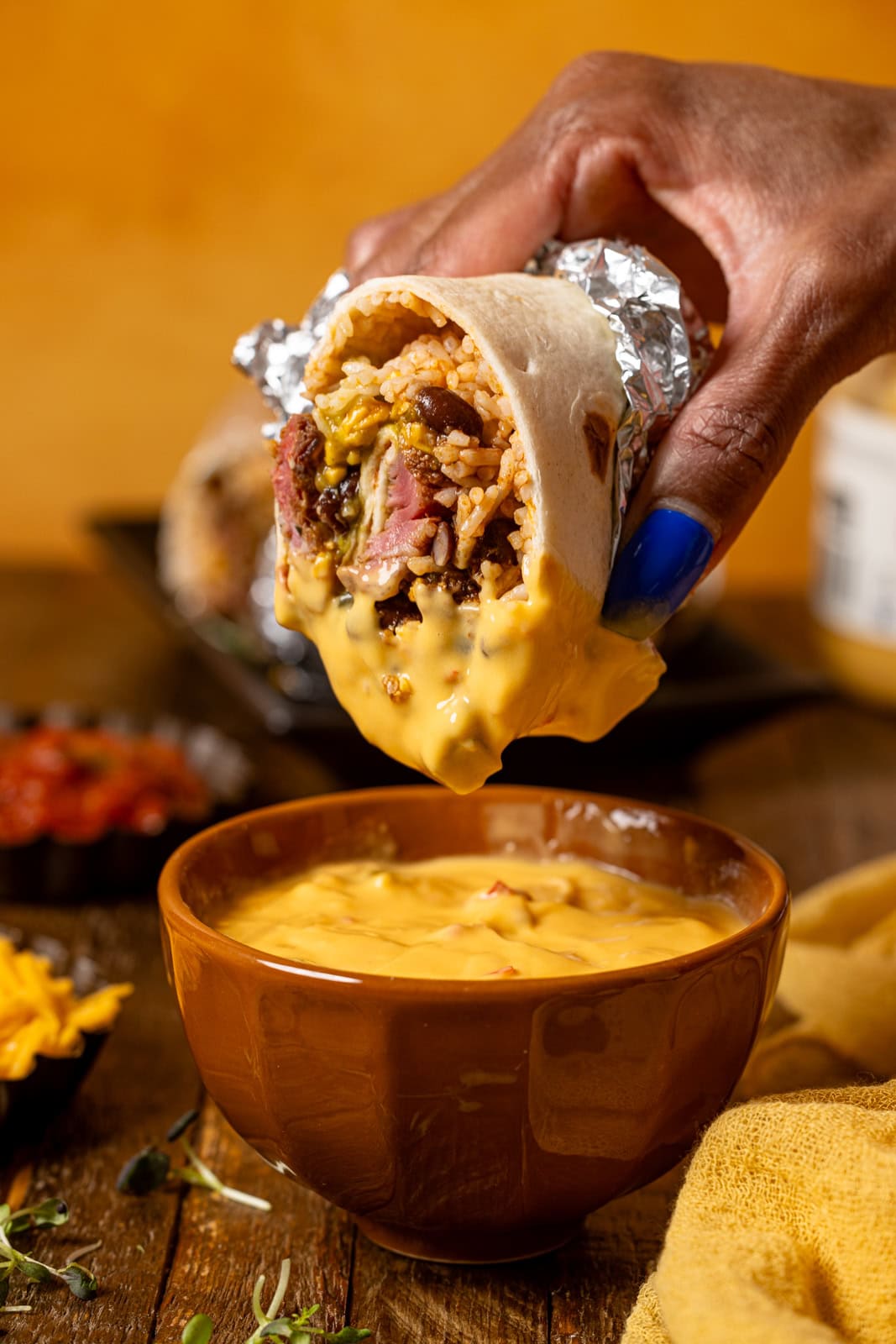 Burrito being held and dipped in a sauce. 