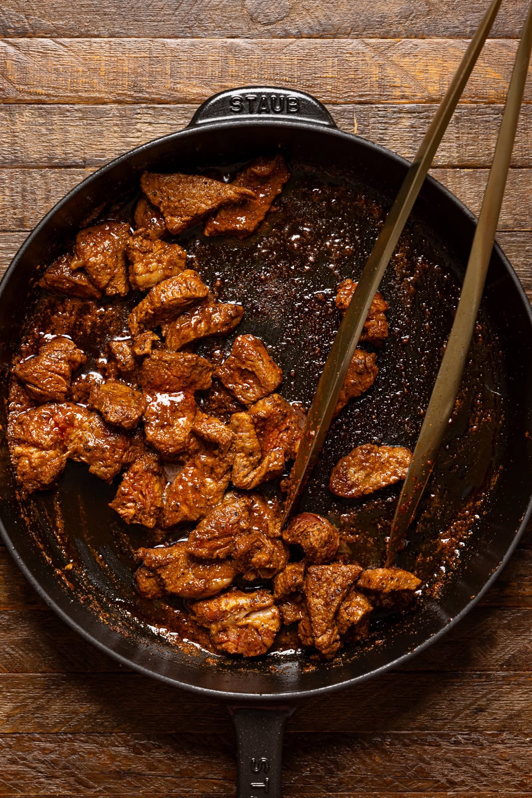 Cooked steak in a skillet with tongs. 