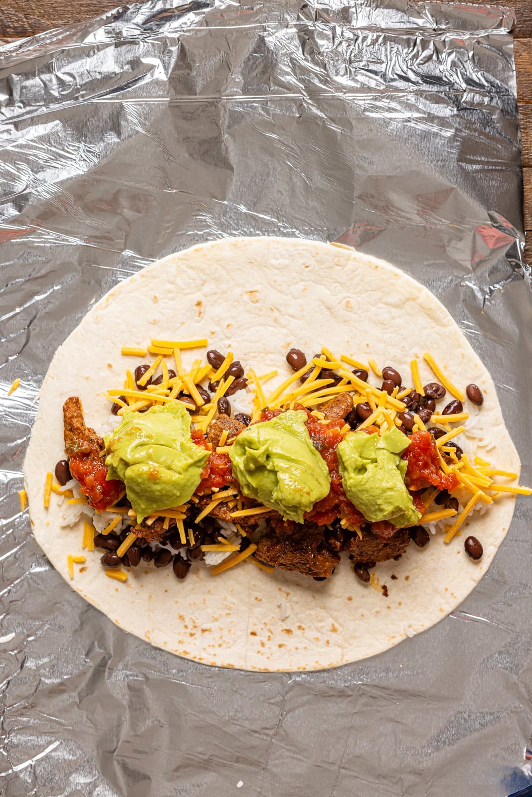 Burrito ingredients on a foil paper layered together. 