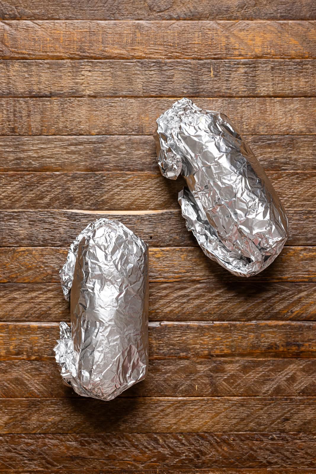 Burritos wrapped up in foil paper on a brown wood table.
