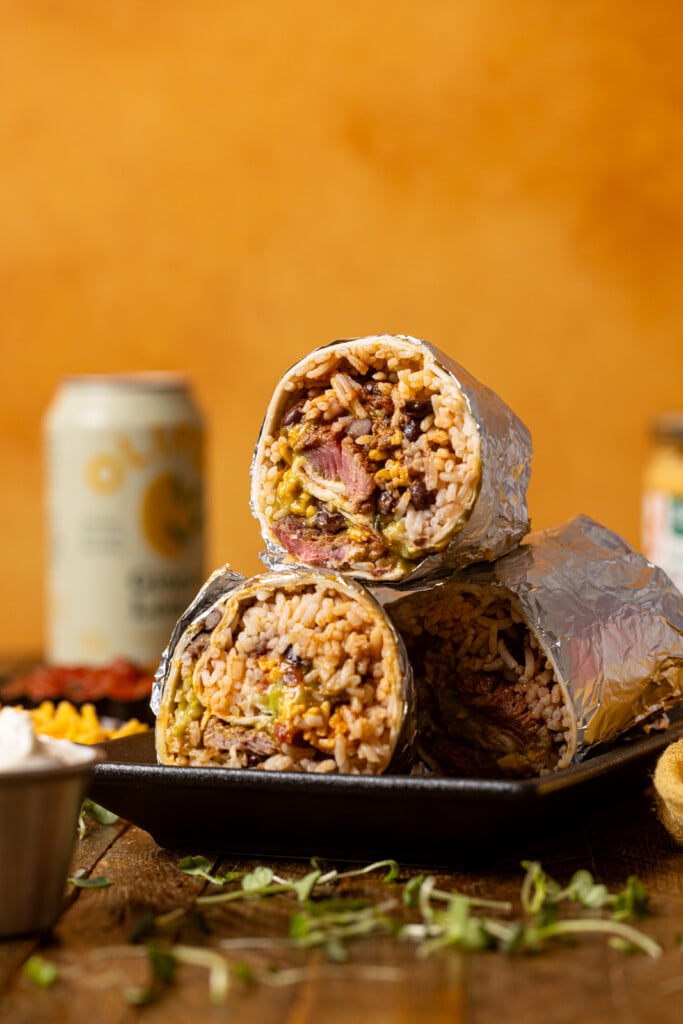 Steak burritos stacked on a platter with an orange background.