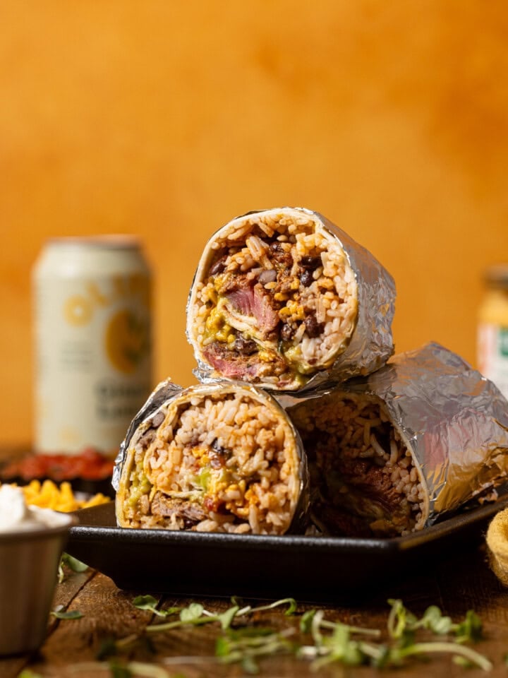 Steak burritos stacked on a platter with an orange background.