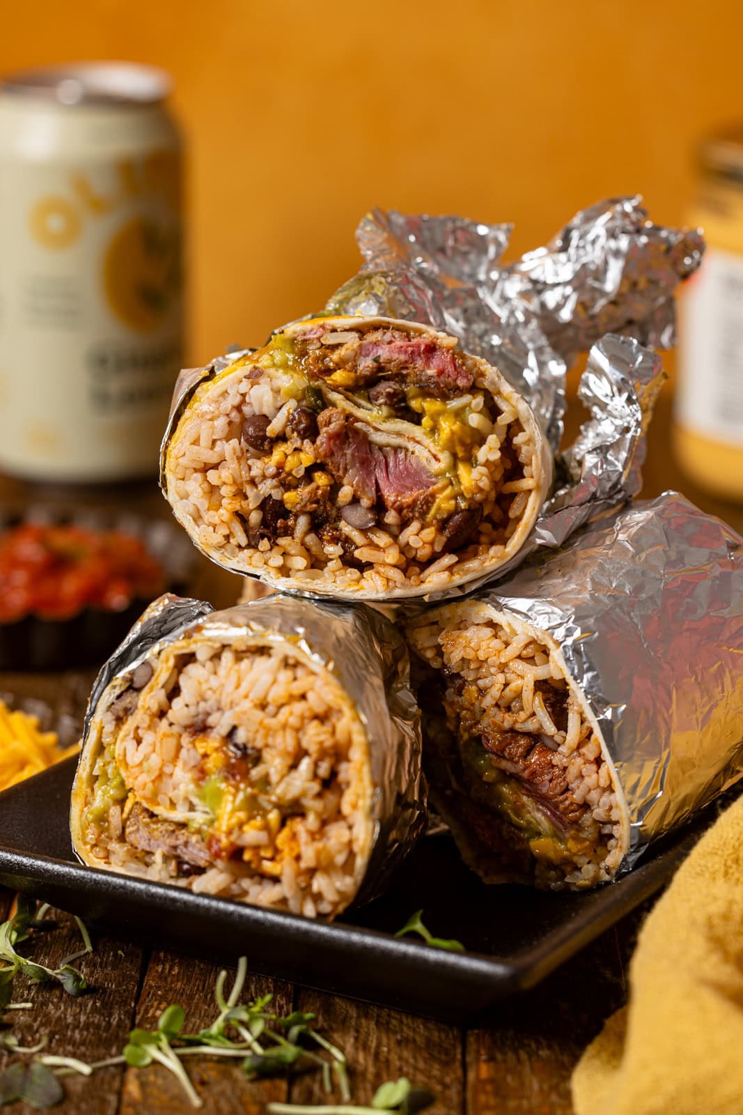 Stacked burritos on a platter with drinks and dips.