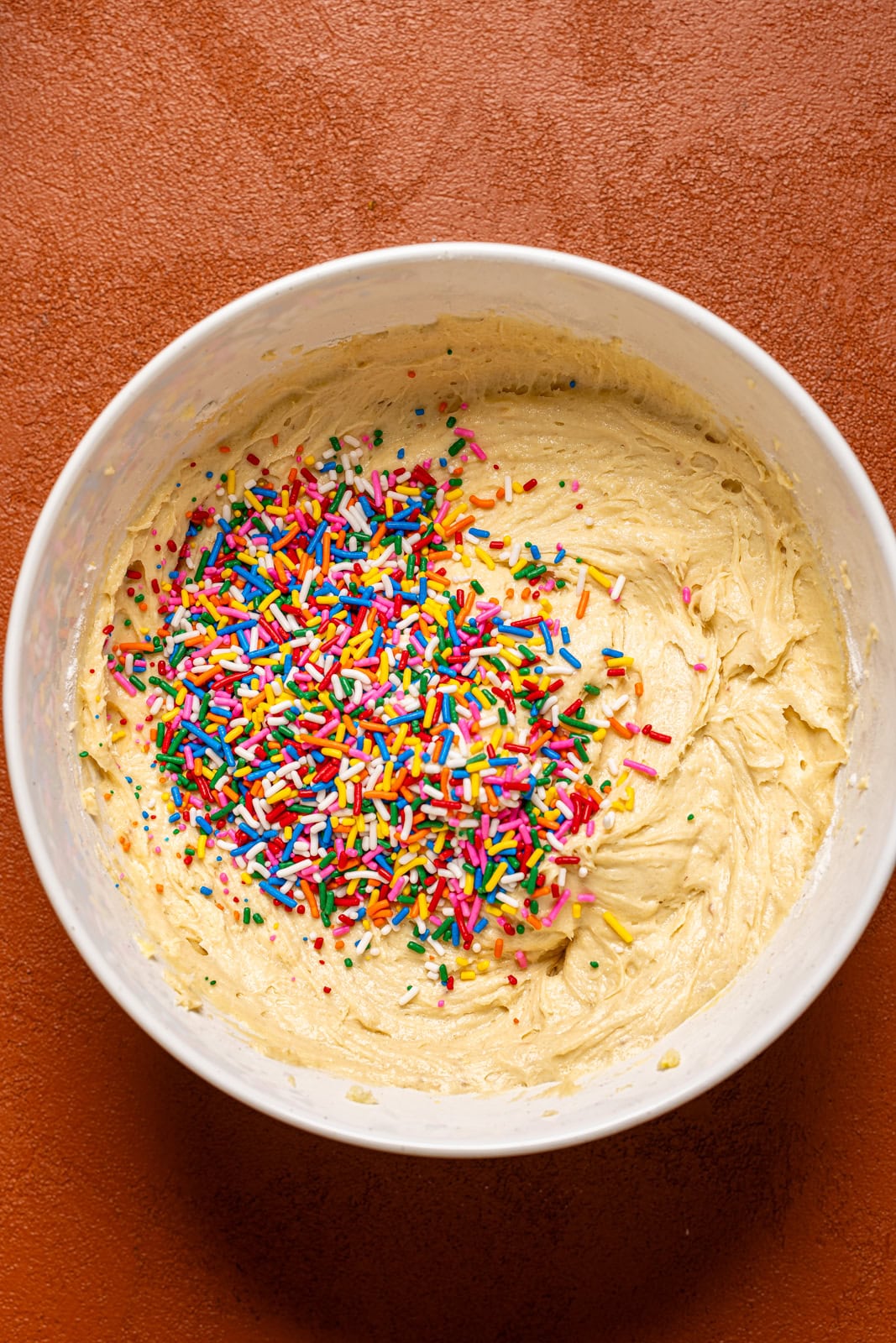 Cake batter in a white bowl with sprinkles. 