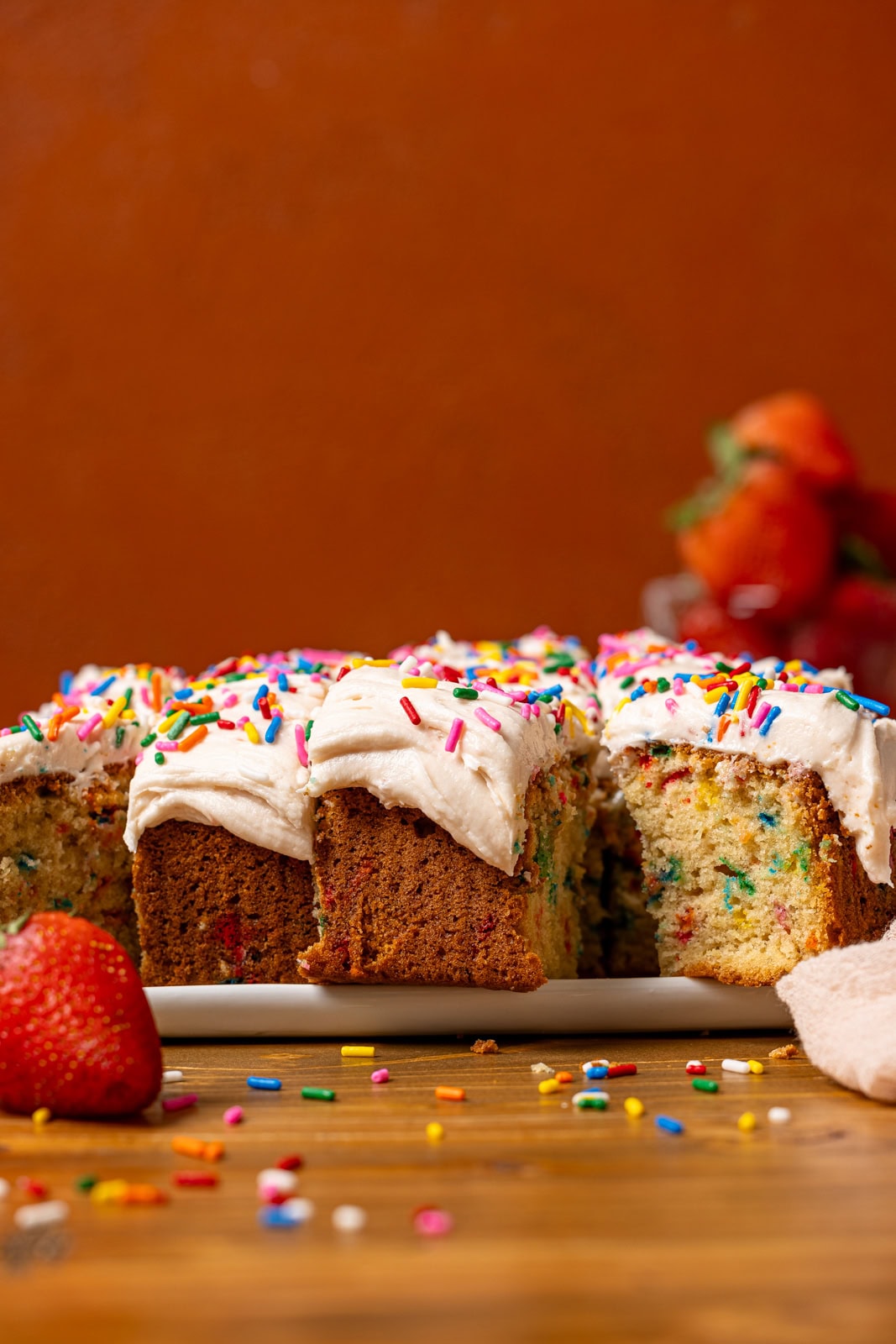 Sliced cake with strawberries in the background. 