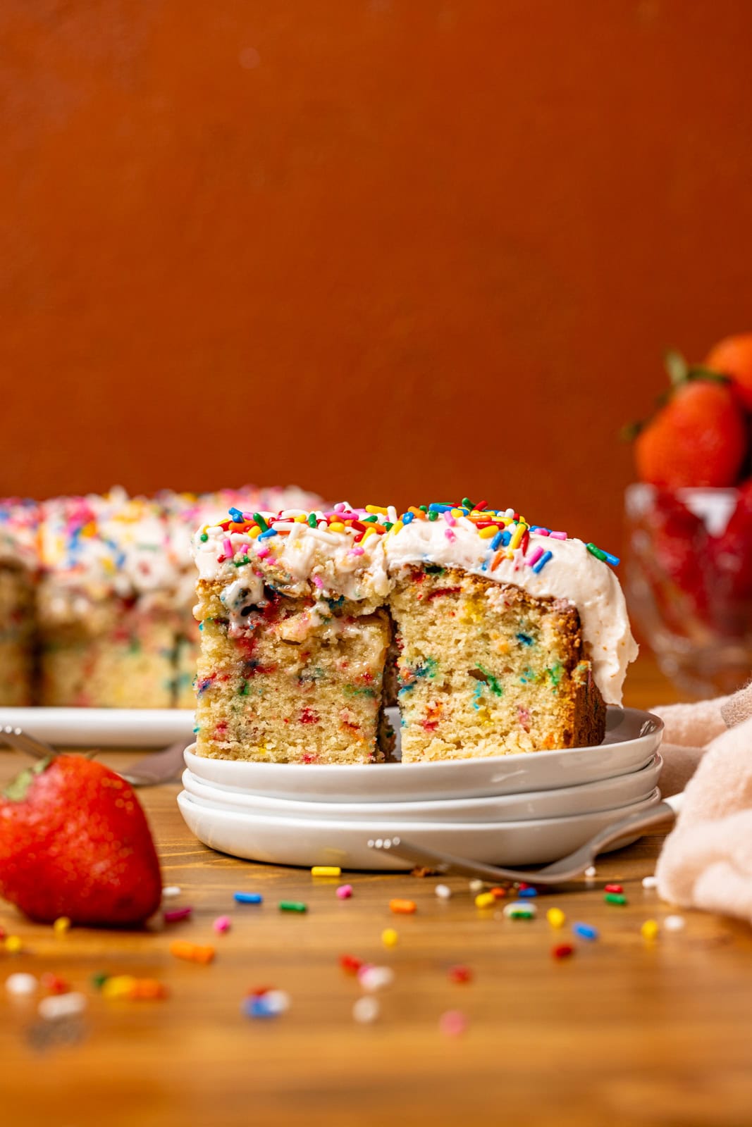 Cake slices on a stack of white plates with strawberries. 