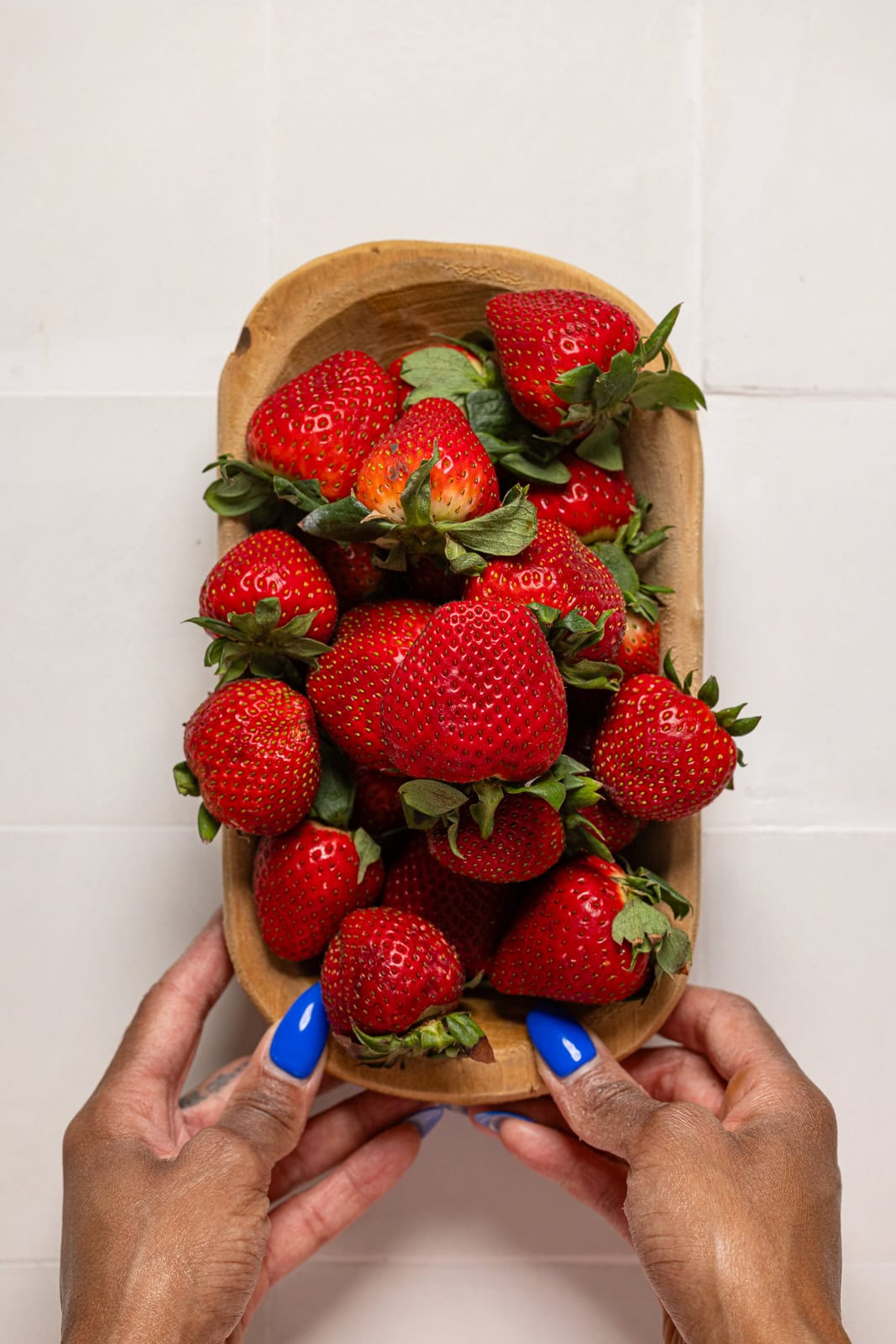 Wooden bowl full of strawberries being held.
