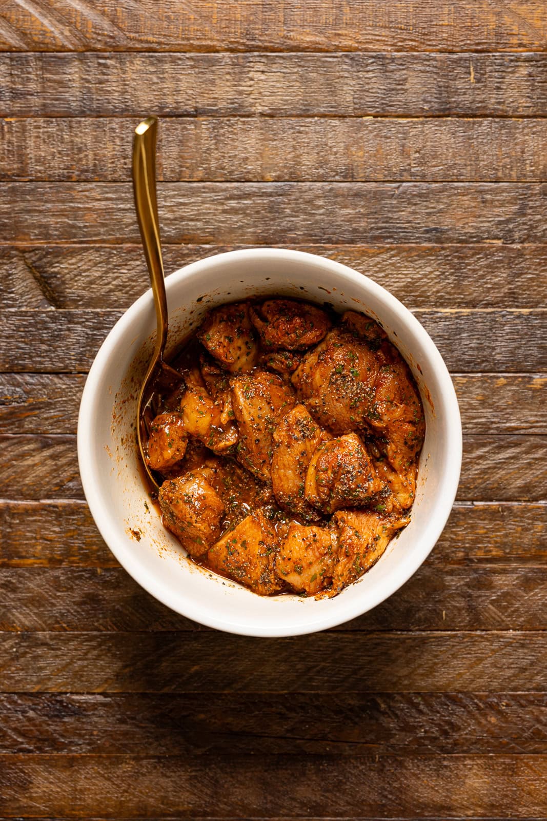 Seasoned + marinated chicken in a bowl with a spoon.