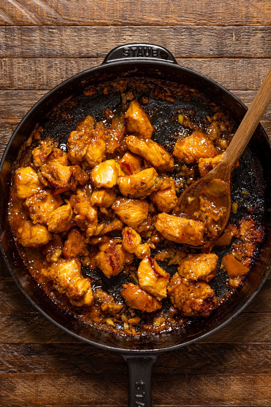 Cooked chicken in a black skillet with a wooden spoon.