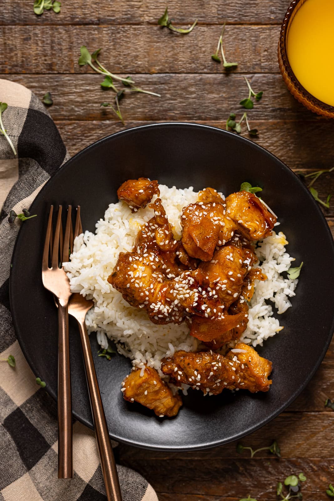 Orange chicken in a black plate with forks and juice.