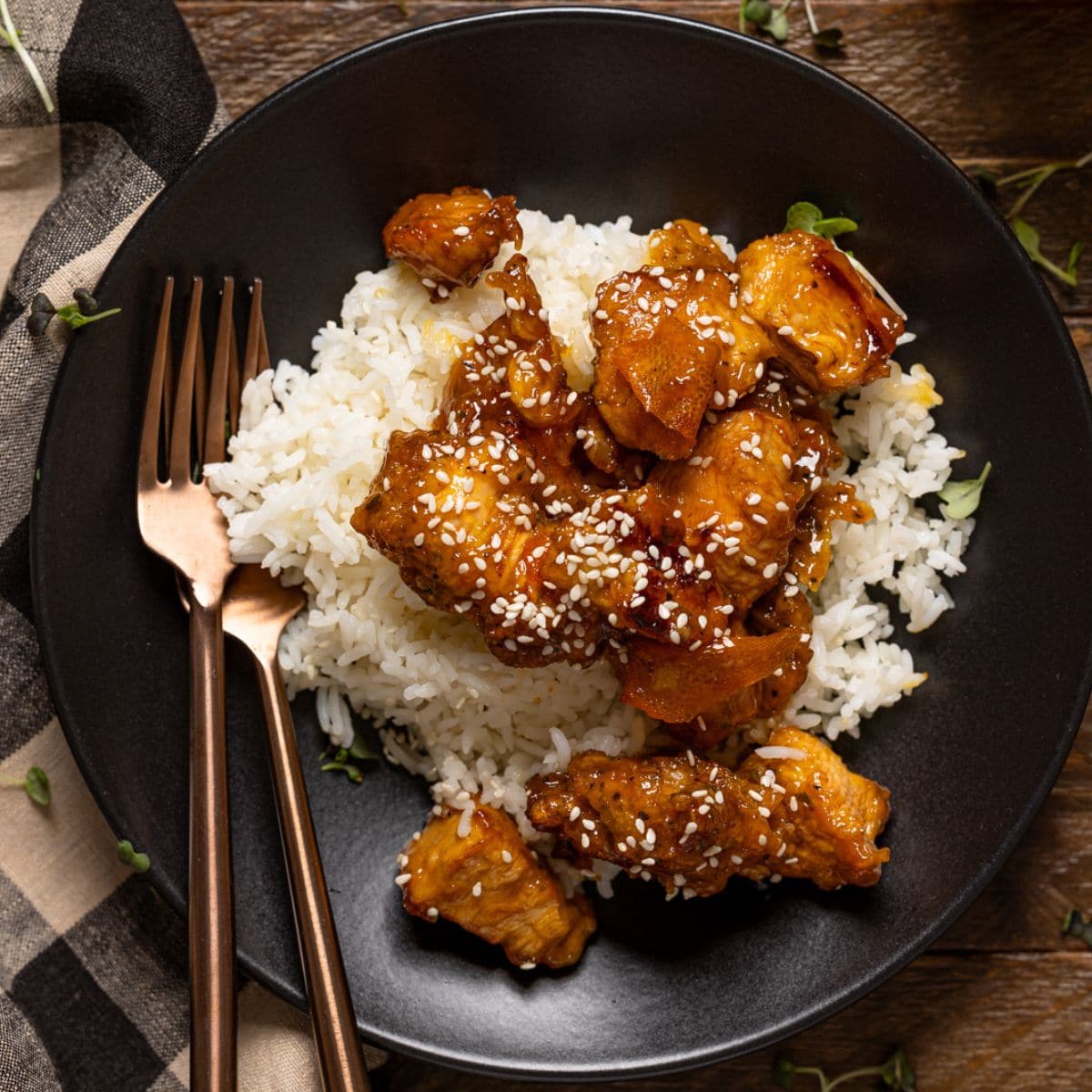 Orange chicken in a black plate with forks and juice.
