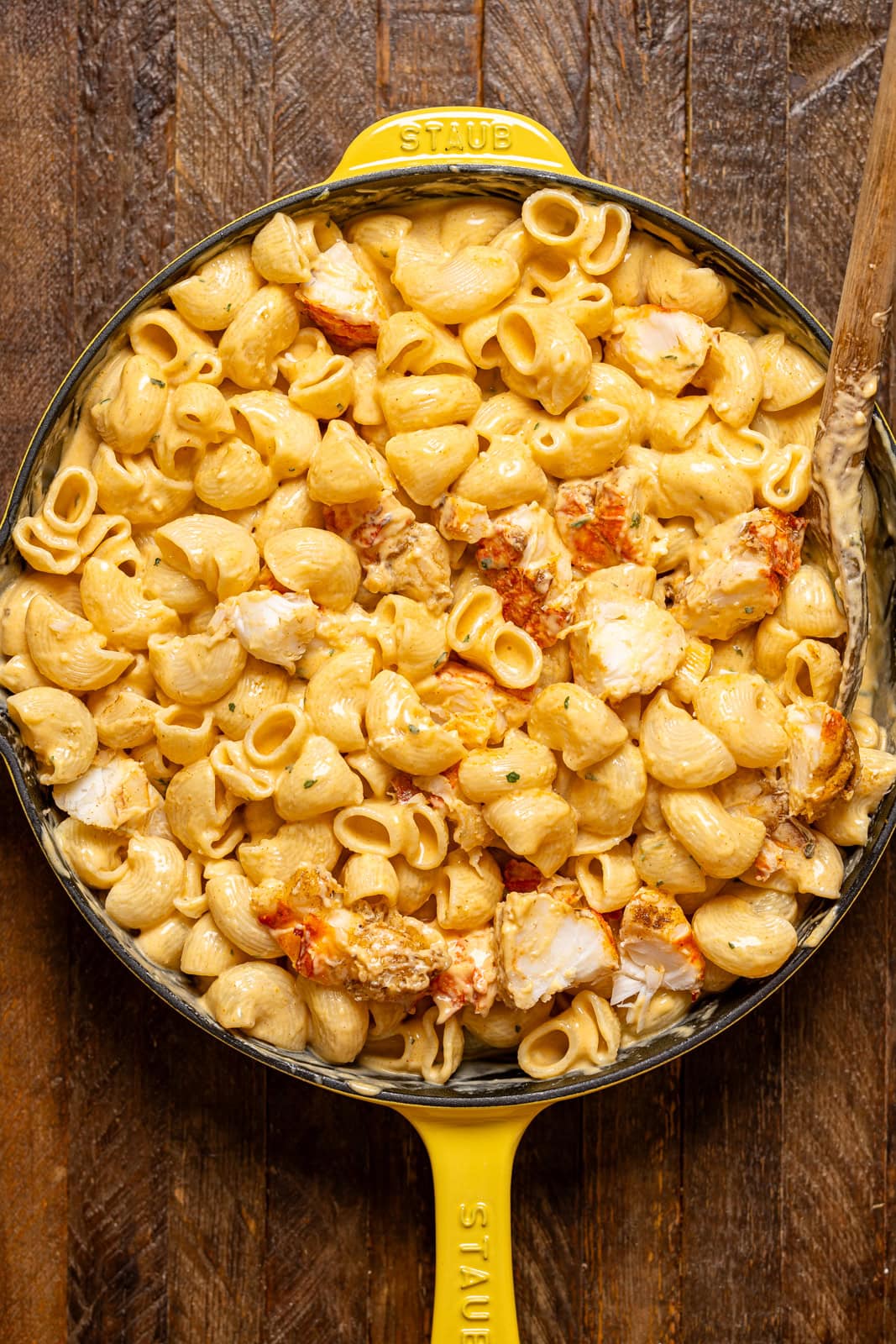 All mac and cheese ingredients together in a yellow skillet with a wooden spoon.