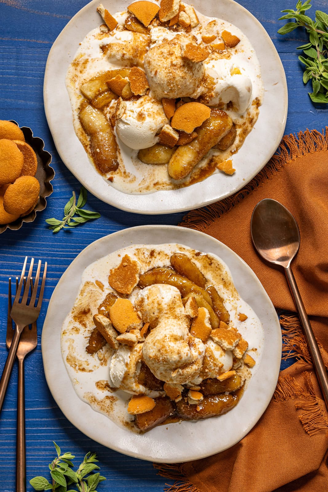 Two plates of bananas foster with a spoon, fork, and side of cookies.
