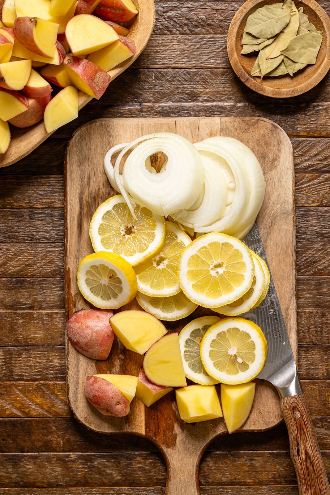 Onions, lemons, and potatoes chopped on a cutting board with a knife.