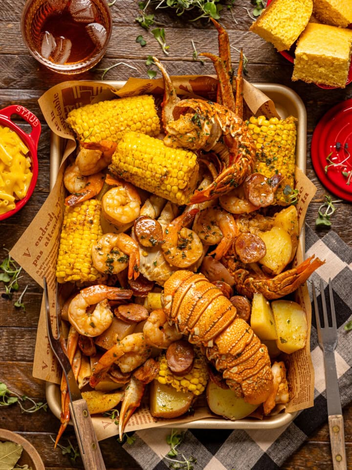 Seafood boil on a baking sheet with a side of mac and cheese, drink, and cornbread.