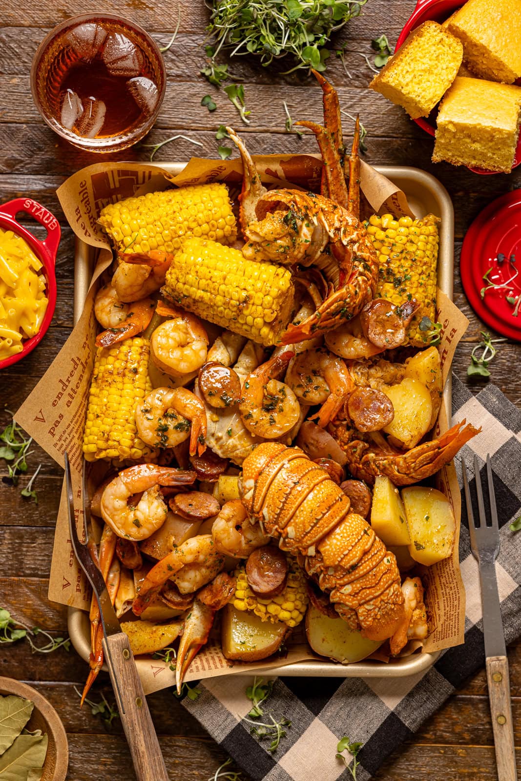 Seafood boil on a baking sheet with a side of mac and cheese, drink, and cornbread.