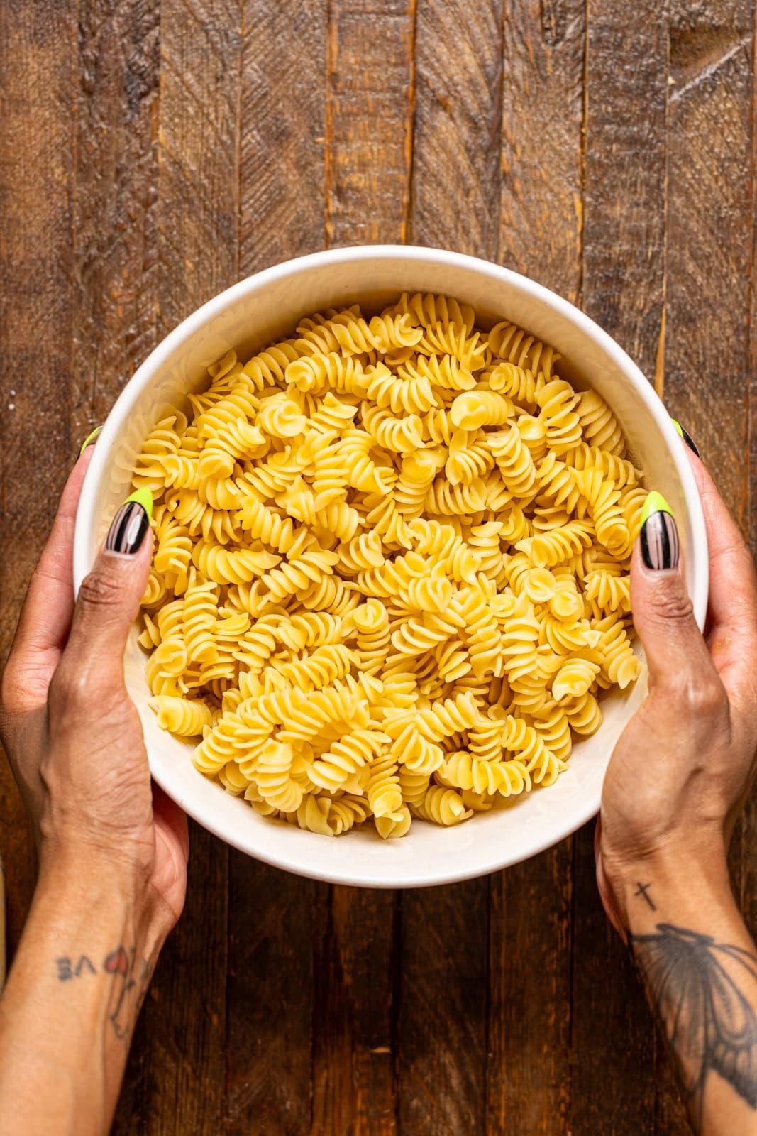 Cooked pasta in a bowl being held on a brown wood table.