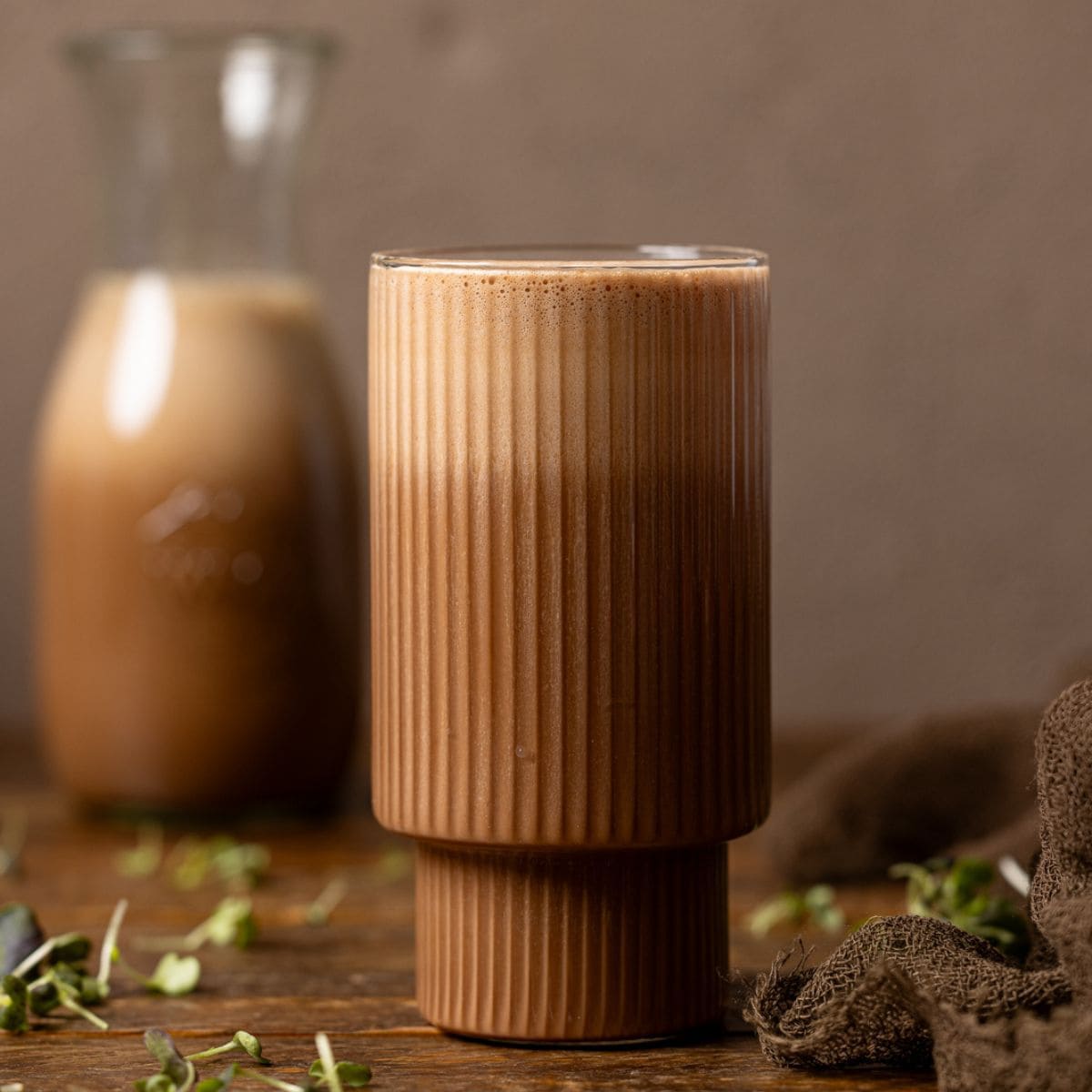 Chocolate milk in a glass and jar on a brown wood table.