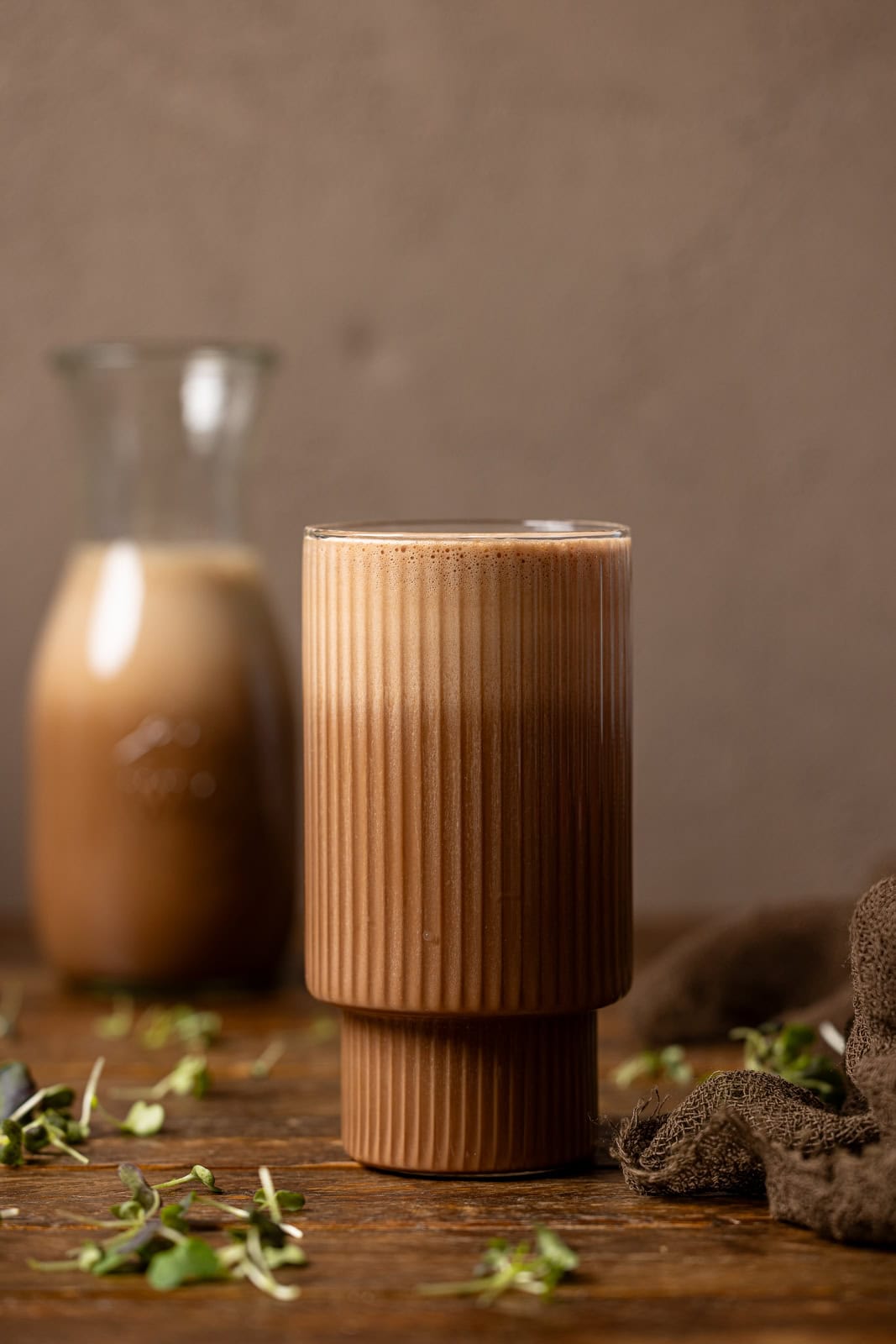 Chocolate milk in a glass and jar on a brown wood table.