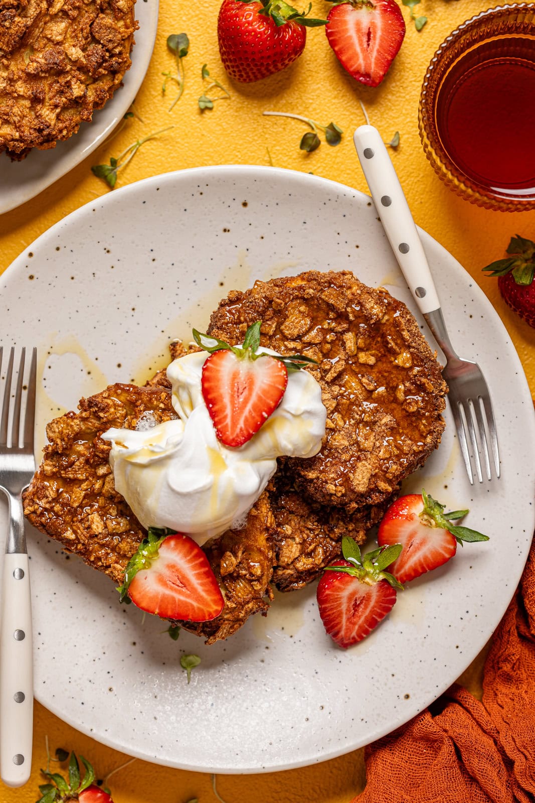 French toast on a plate with strawberries, whipped cream, and two forks.