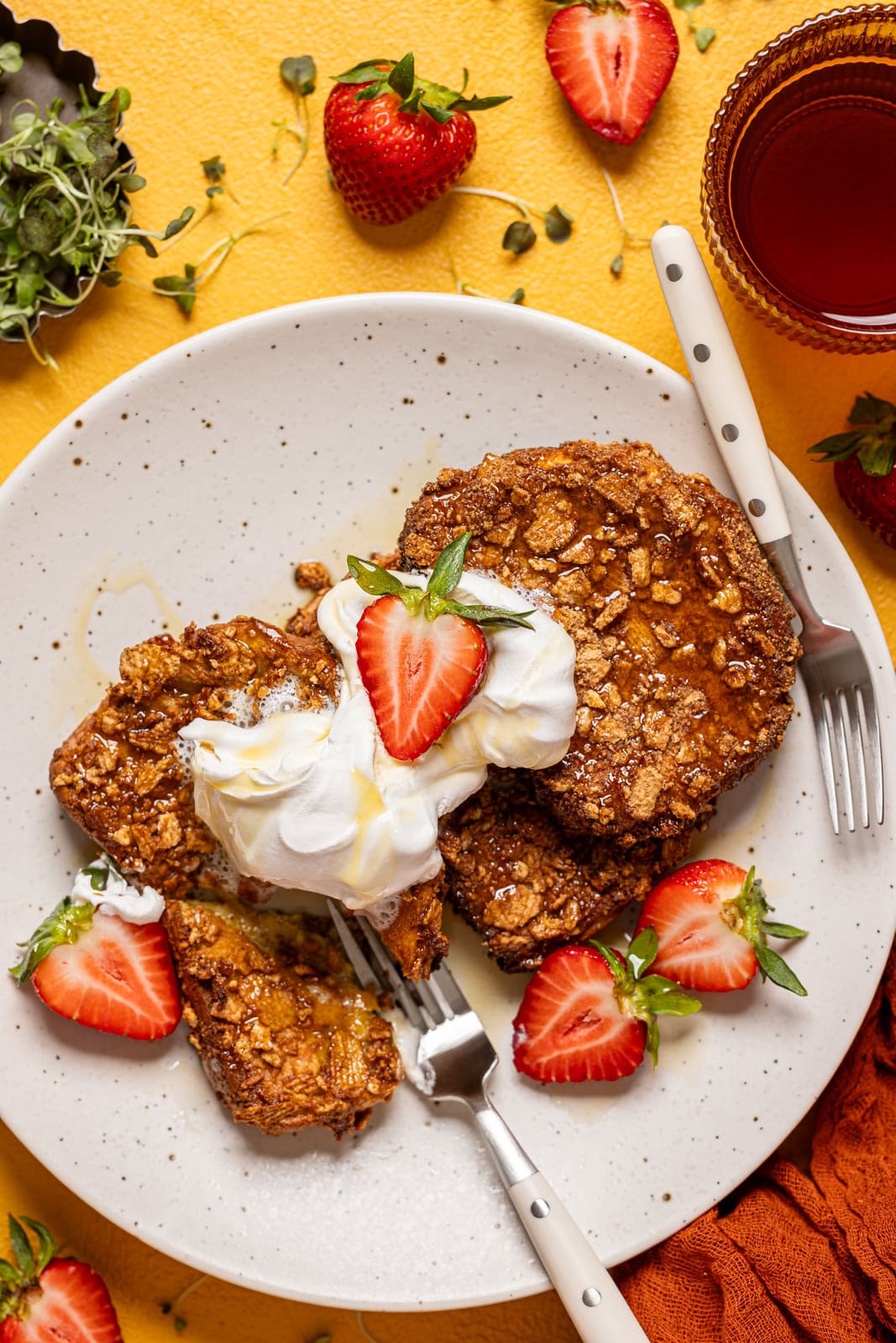 French toast on a plate with two forks, a drink and strawberries.
