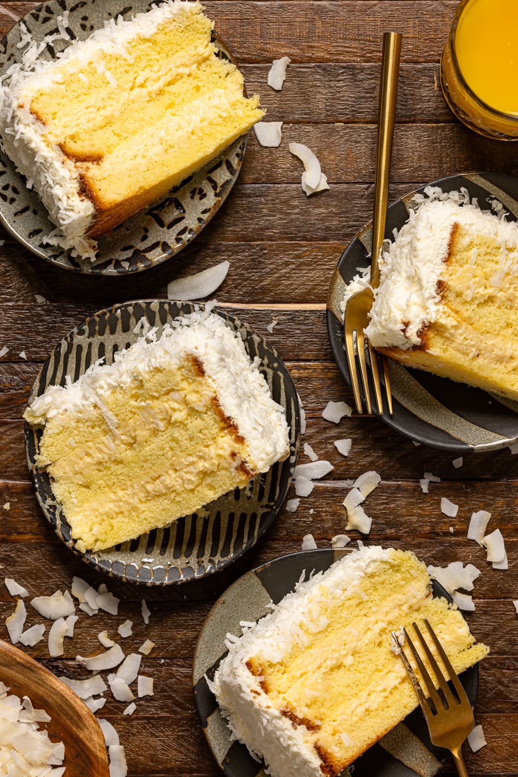 Four slices of cake on plates with forks and coconut flakes.