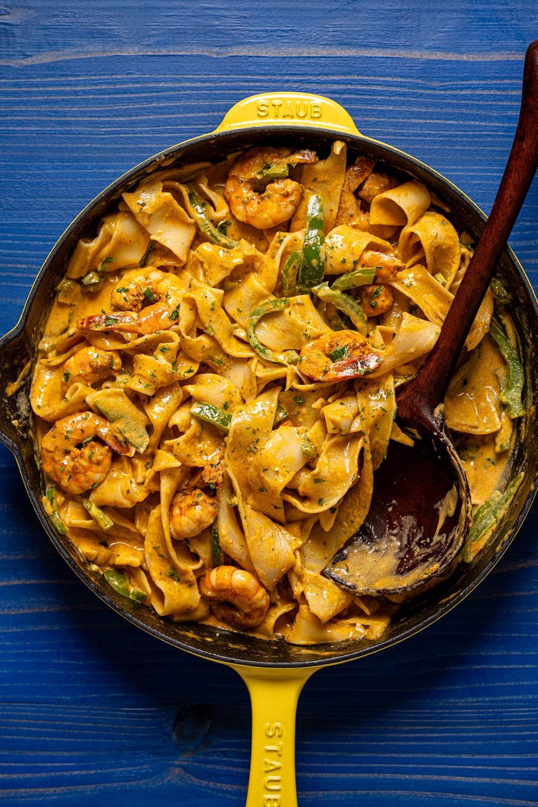Shrimp pasta in a yellow skillet with a wooden spoon.