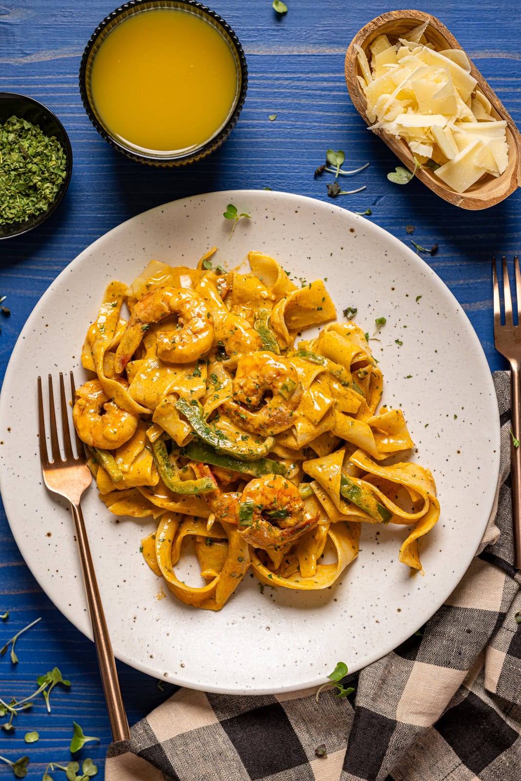 Shrimp pasta on a white plates with a fork, drink, and parmesan.