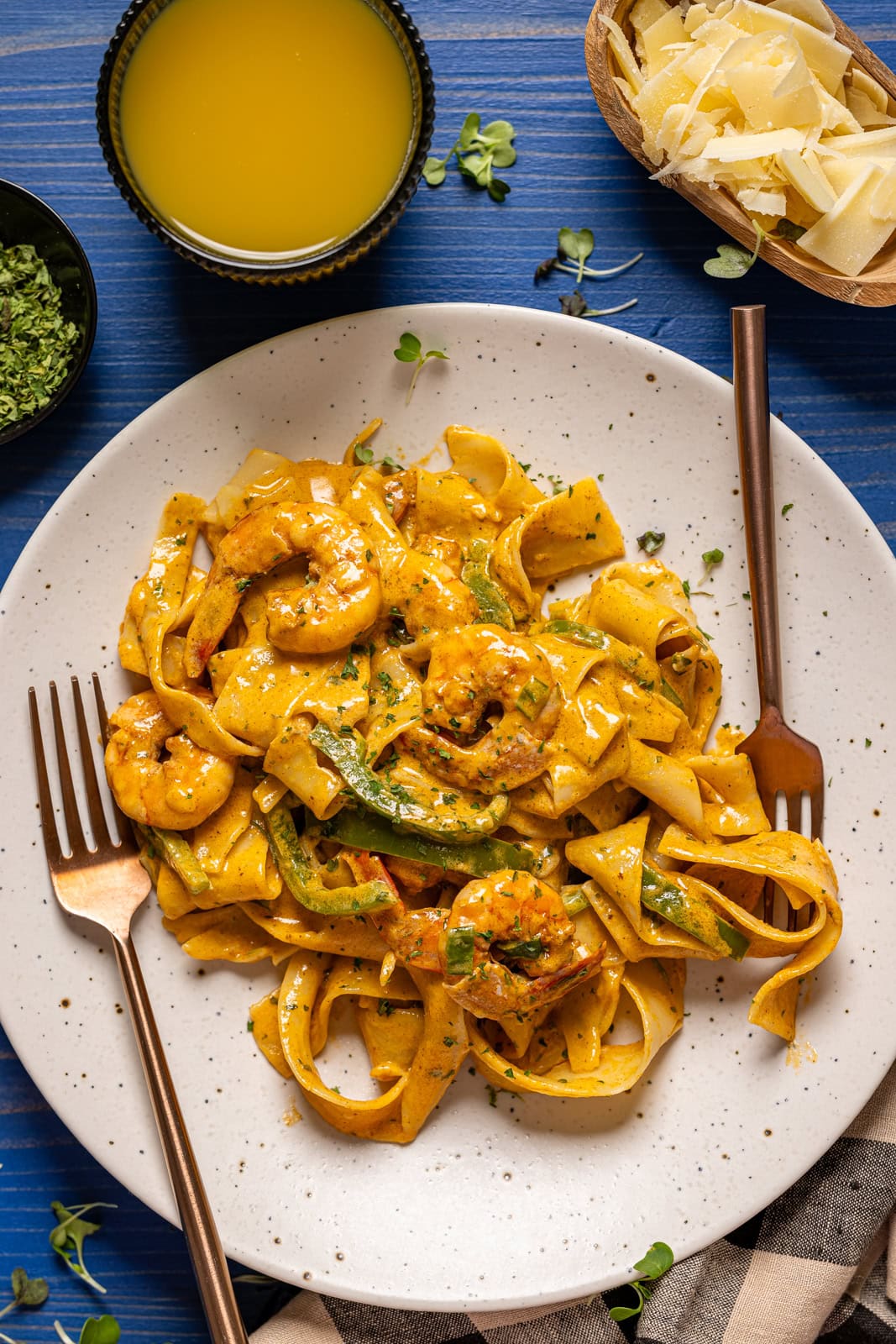 Shrimp pasta on a white plates with two forks and a side of drink.