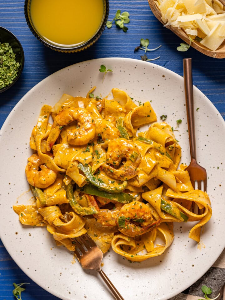 Shrimp pasta on a white plate with two forks on a blue wood table.