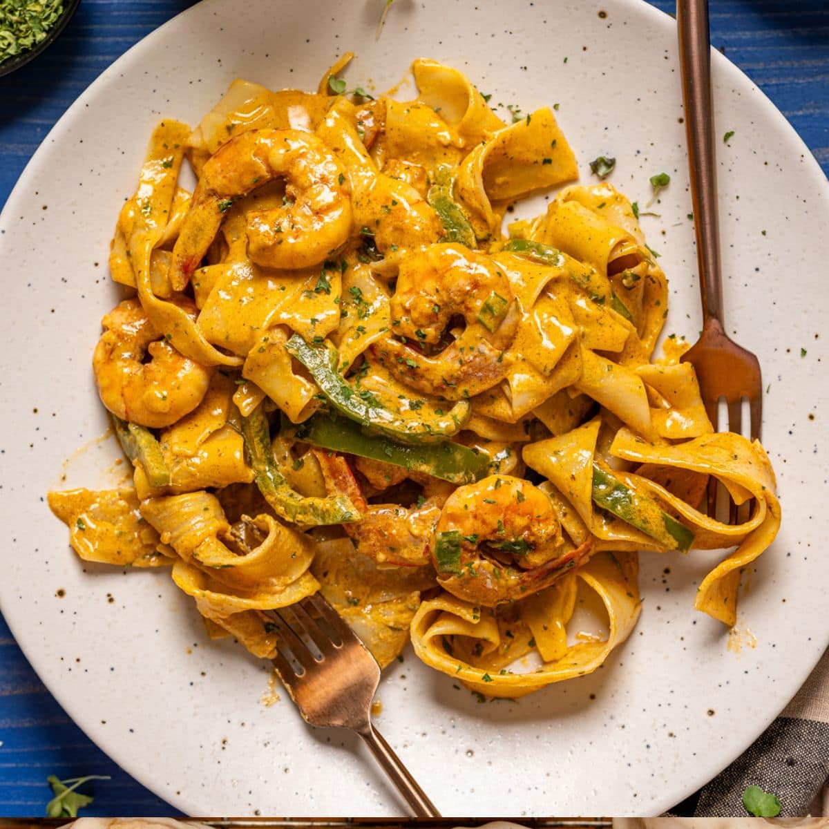 Shrimp pasta on a white plate with two forks on a blue wood table.