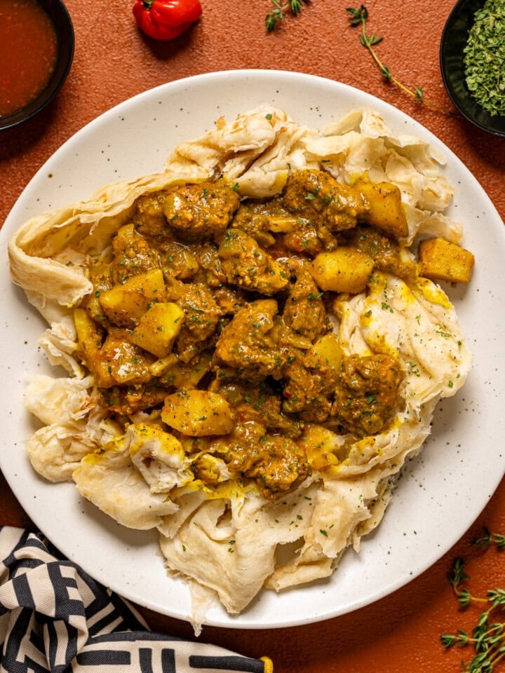 Curry chicken roti on a white plate on a burnt orange table.