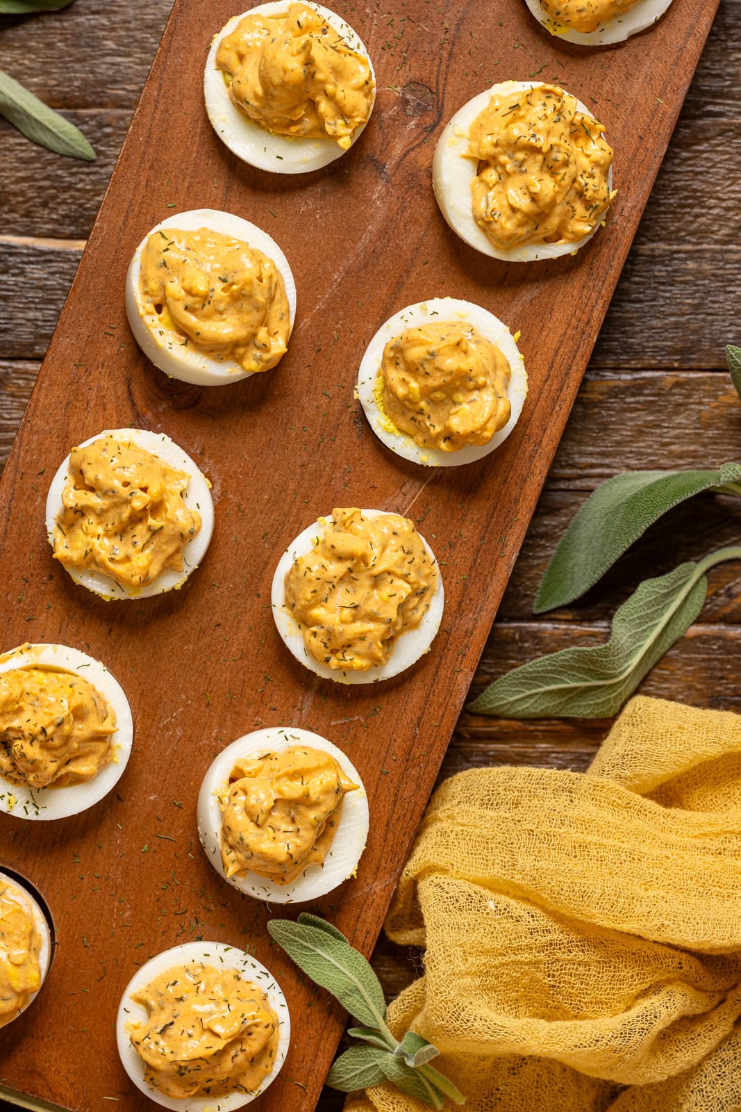 Image of deviled eggs on a wooden tray with sage leaves.