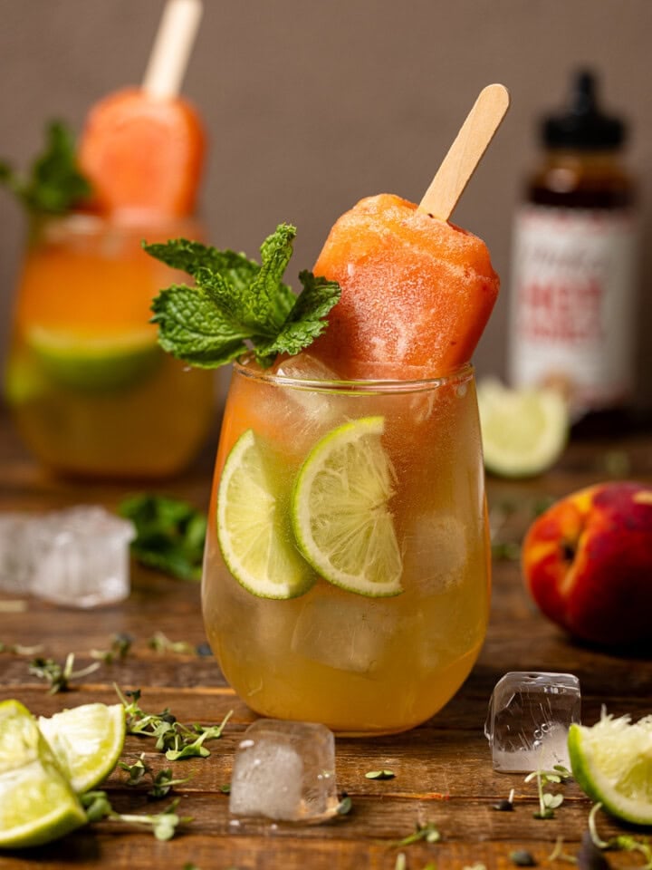 Overview of mocktails in two glasses with lime, a peach, ice cubes, and hot honey.