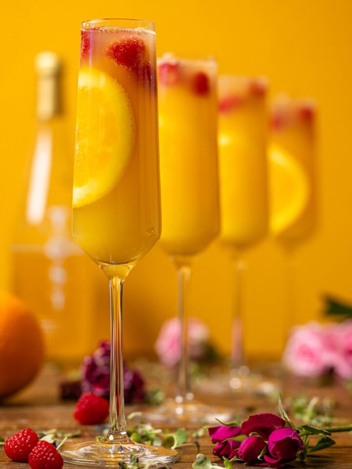 Four glasses of mimosas with flowers and raspberries.