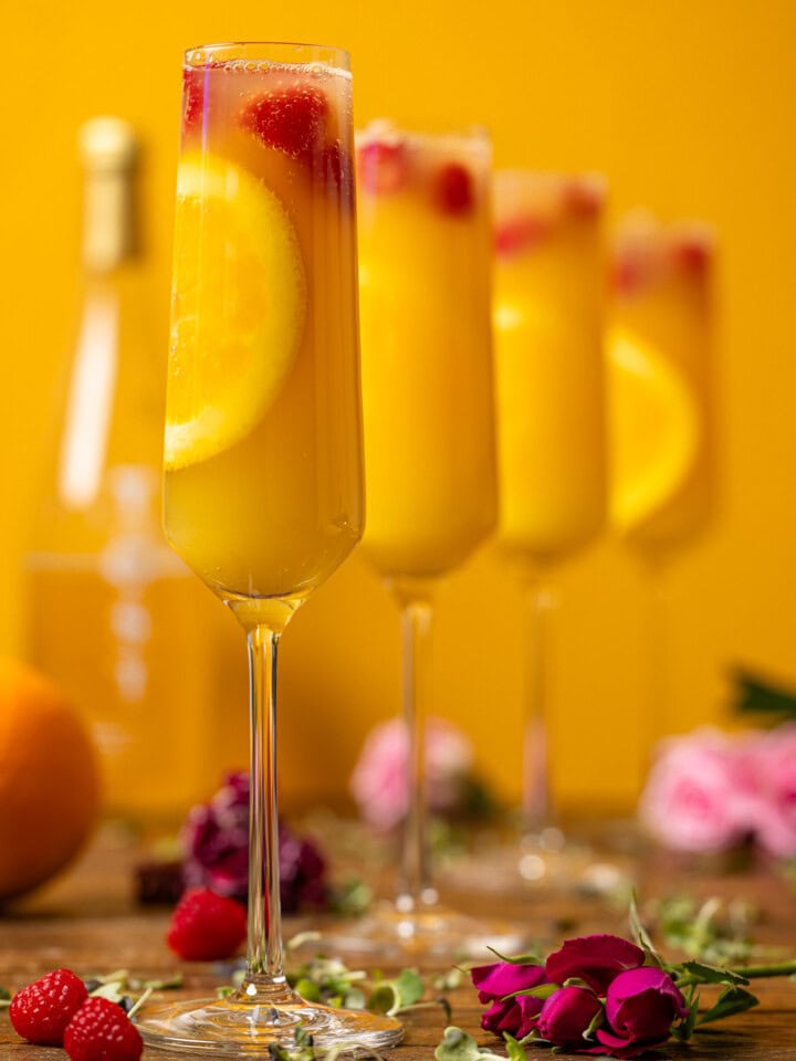 Four glasses of mimosas with flowers and raspberries.