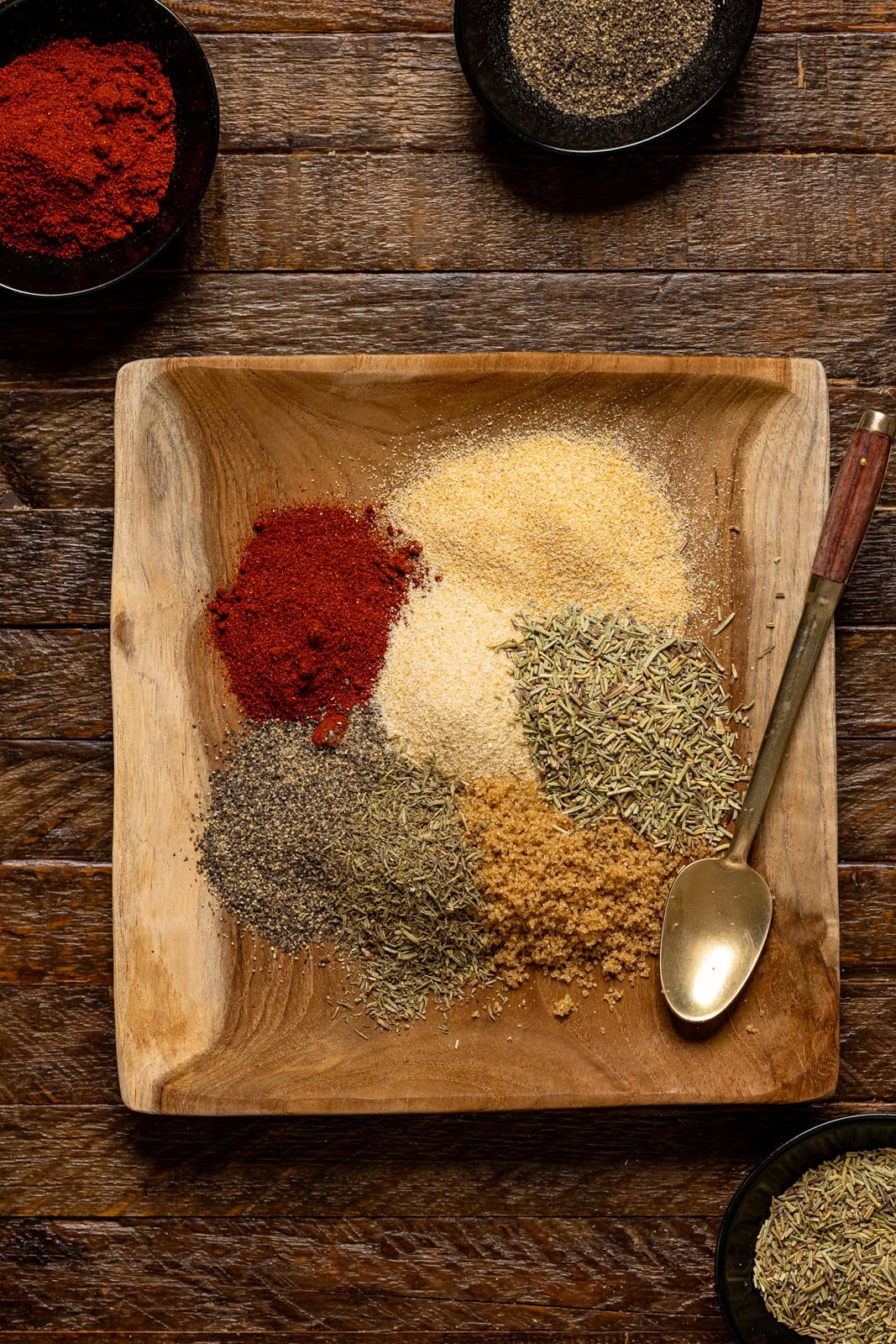 Seasonings on a brown wood plate with a spoon.