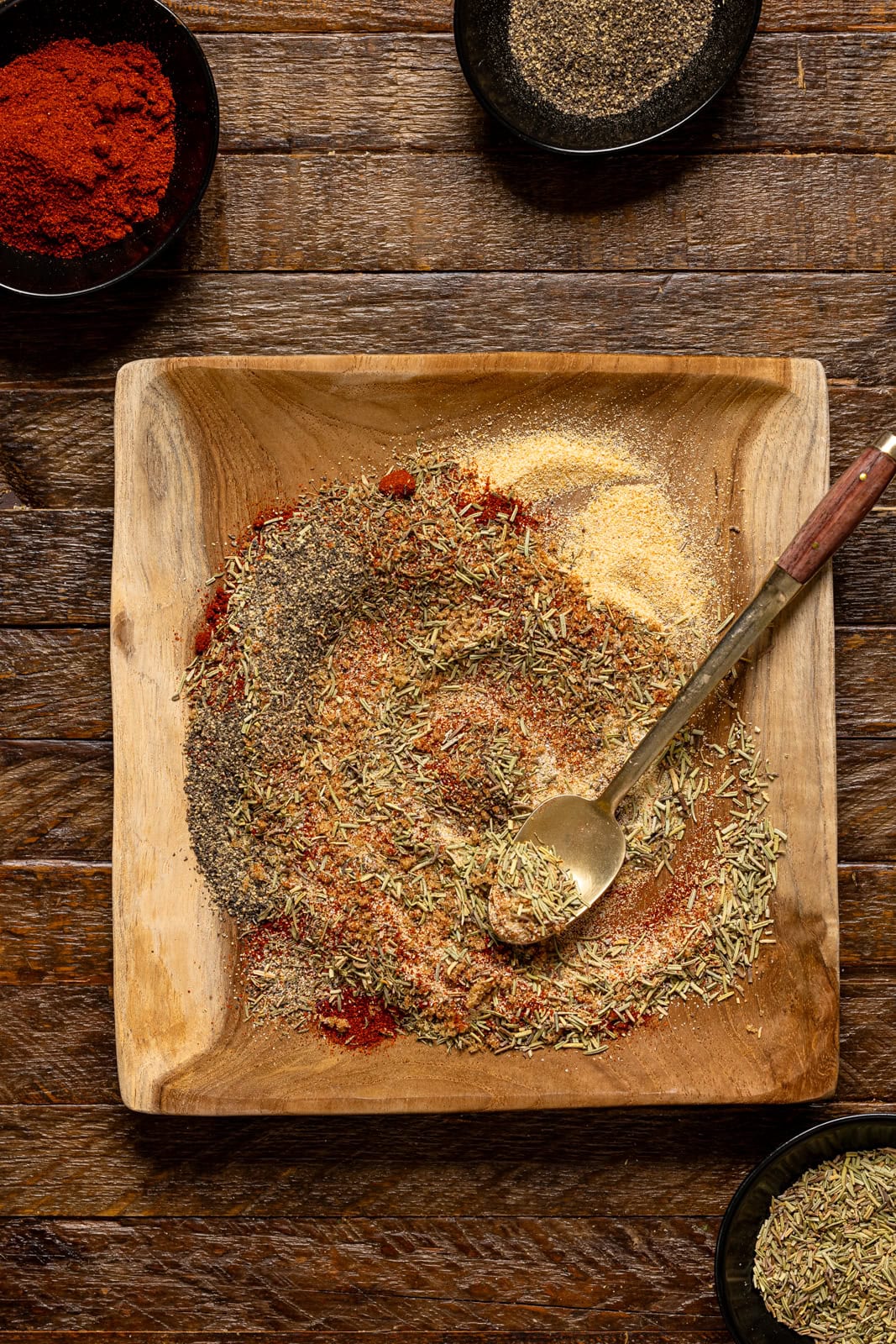Seasonings stirred together on a wood plate with a spoon.