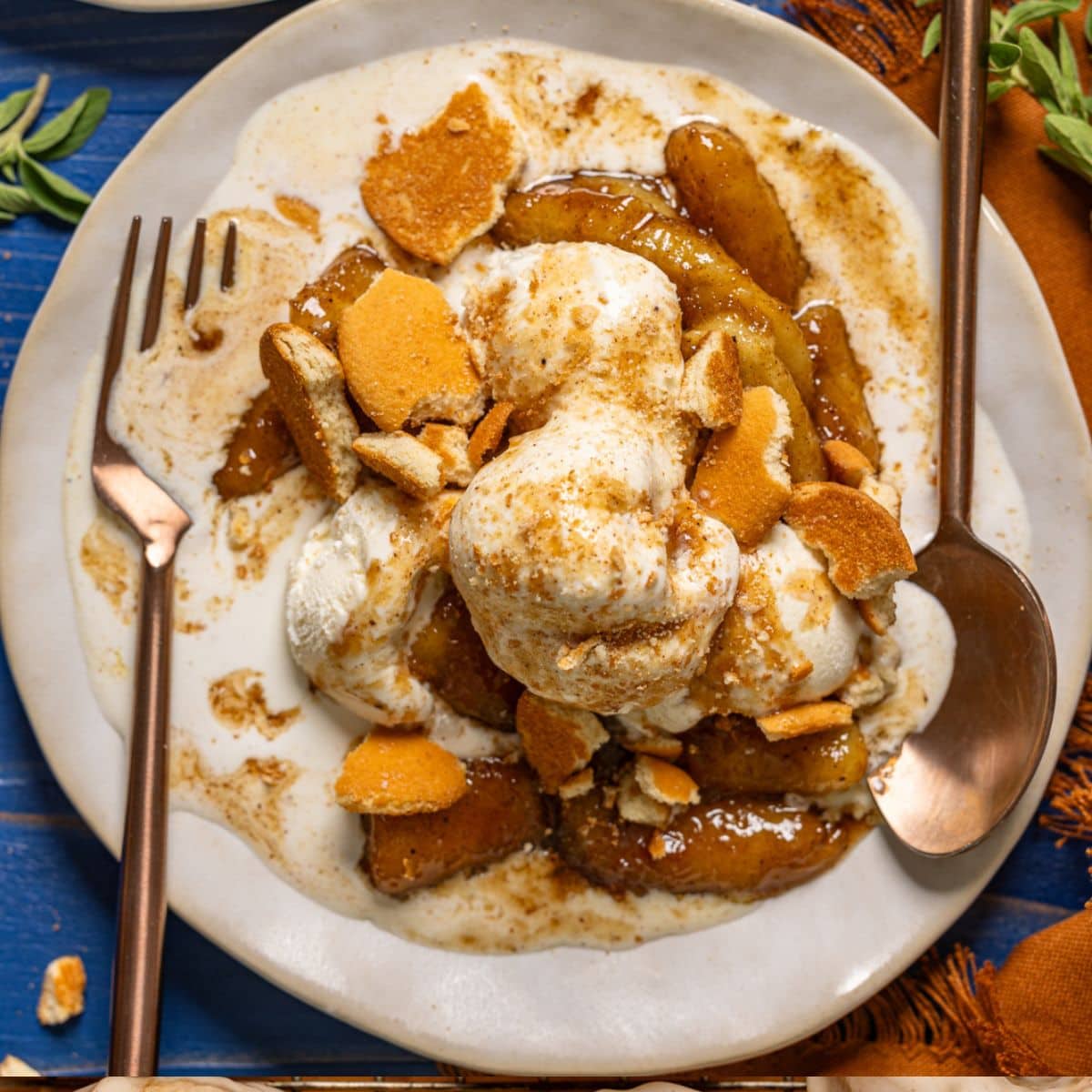 Bananas foster in a white plates with a fork and spoon and cookies on a blue wood table.