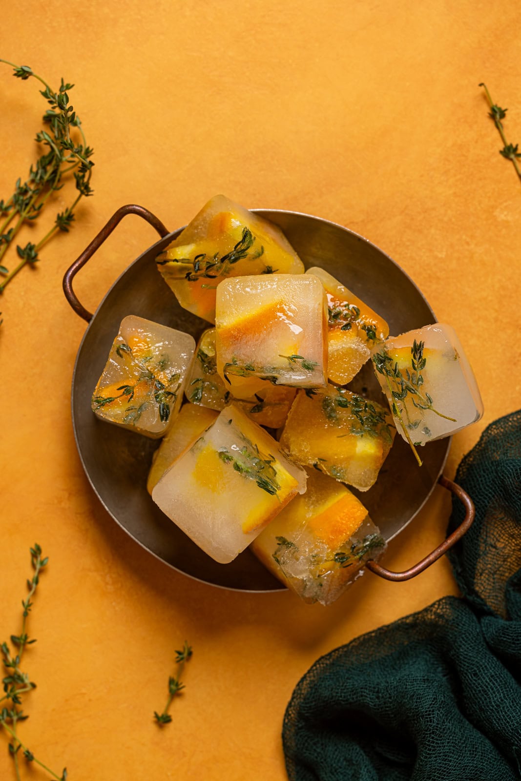 Ice cubes in a metal tray with thyme sprigs.