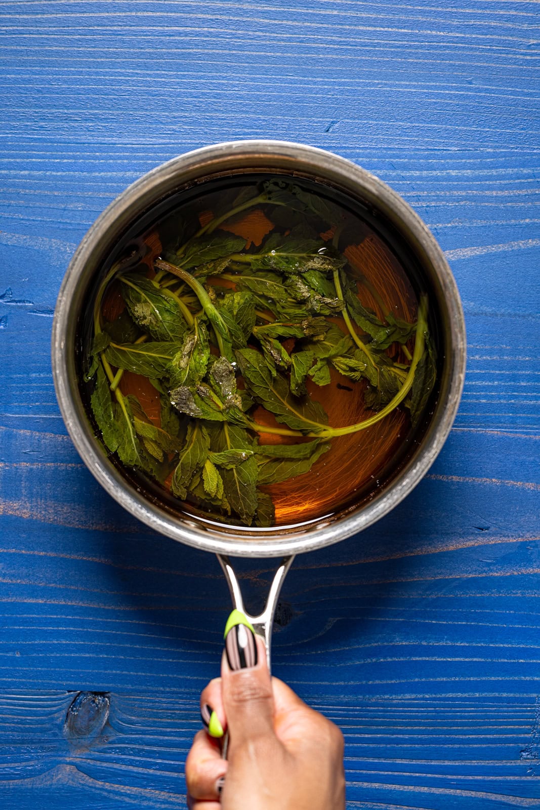 Simple syrup in a silver pot being held on a navy wood table.