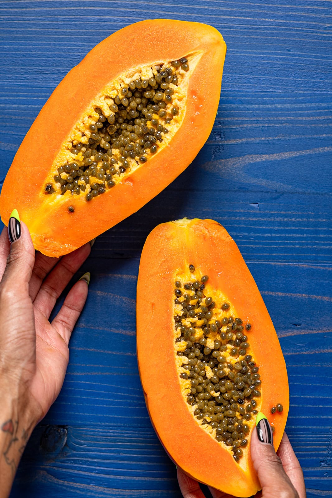 Sliced papaya fruit being held on a navy wood table.