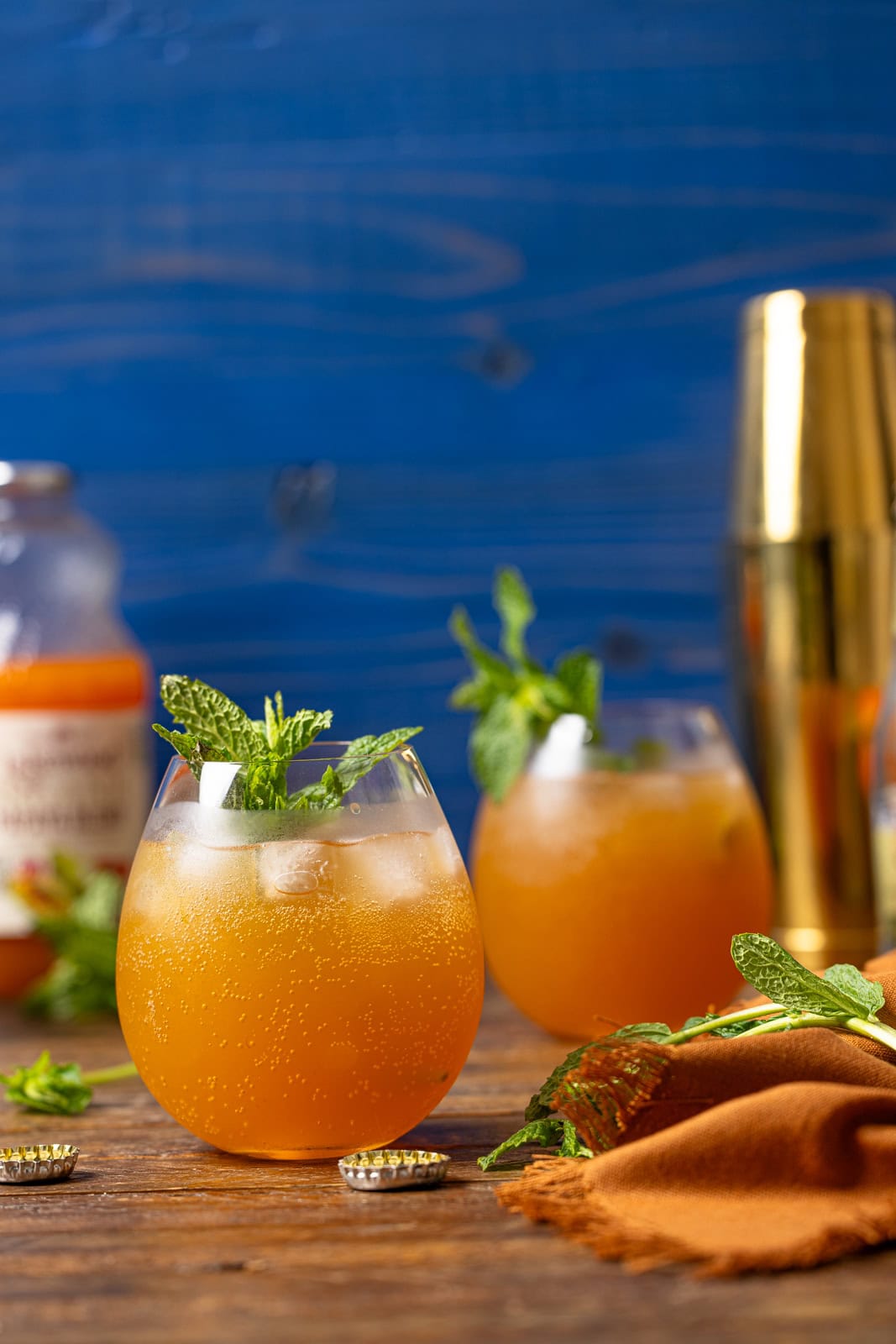 Two glasses of mocktails with juice and a gold cocktail shaker in the background. 
