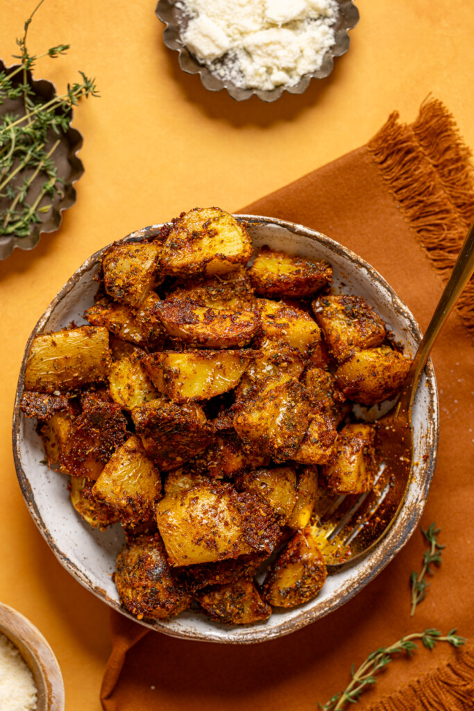 Roasted potatoes in a dish with a spoon and parmesan.