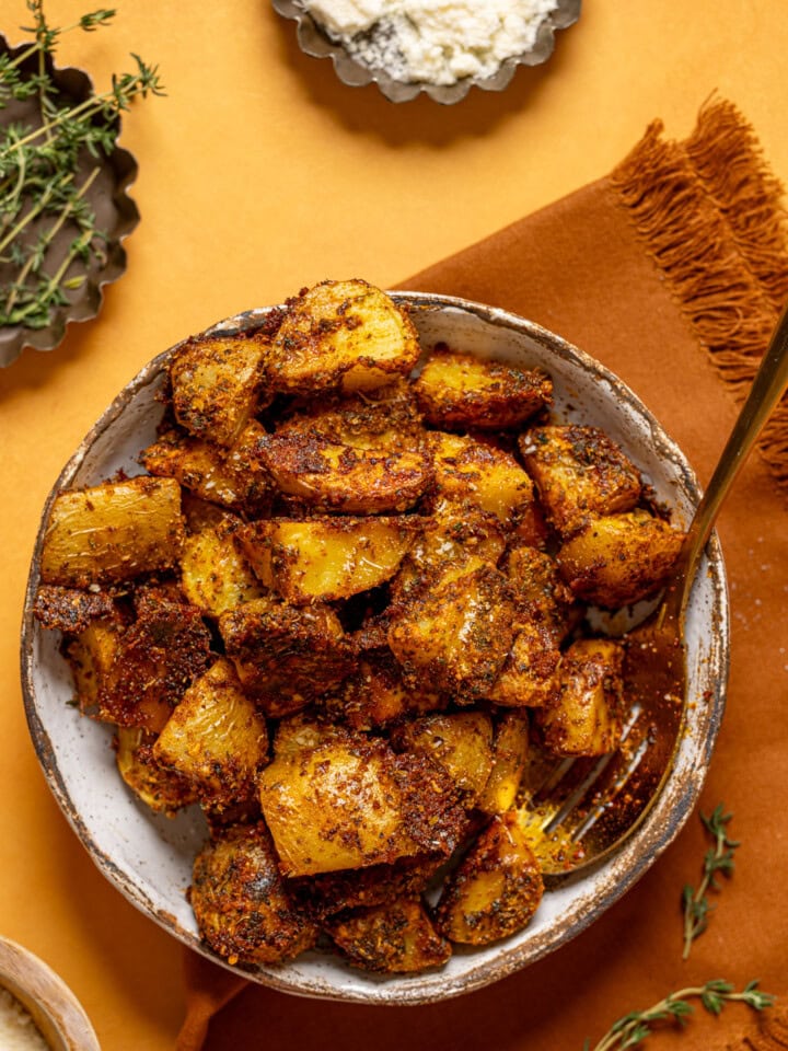 Roasted potatoes in a dish with a spoon and parmesan.