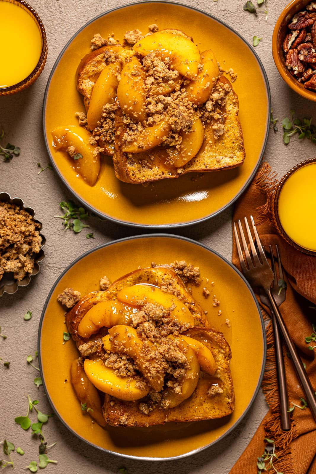 Two plates of french toast on yellow plates with glasses of orange juice and pecans.