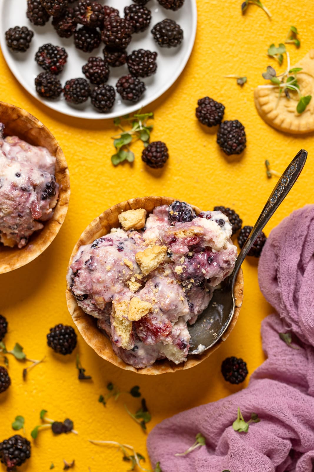 Ice cream in waffle cones with a spoon and blackberries.