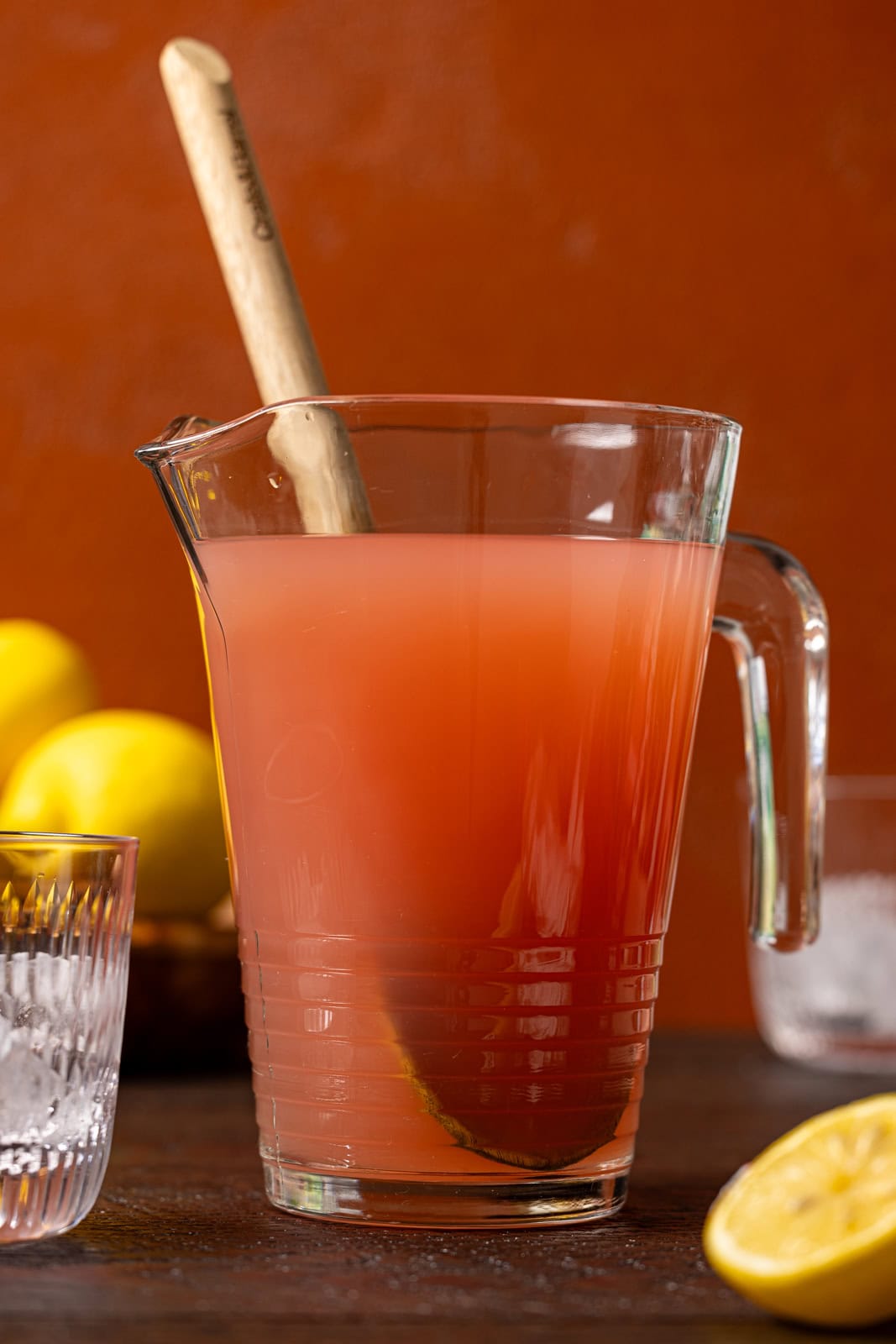 Pitcher of pink lemonade with a wooden spoon and lemons.